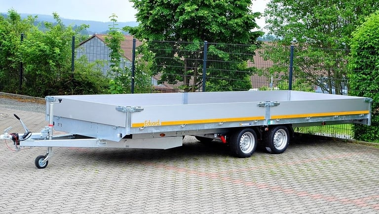 White and yellow flatbed trailer with dual axles parked on a brick surface with trees in the background