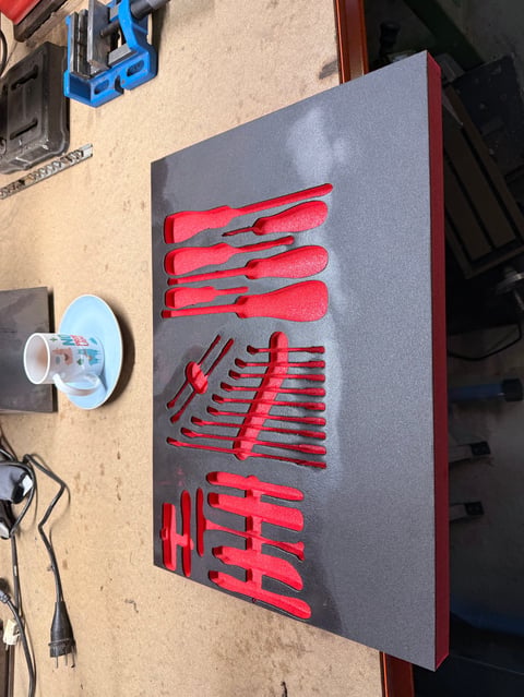 Gray wall-mounted pegboard organizer with red tools and screwdrivers neatly arranged in garage workshop