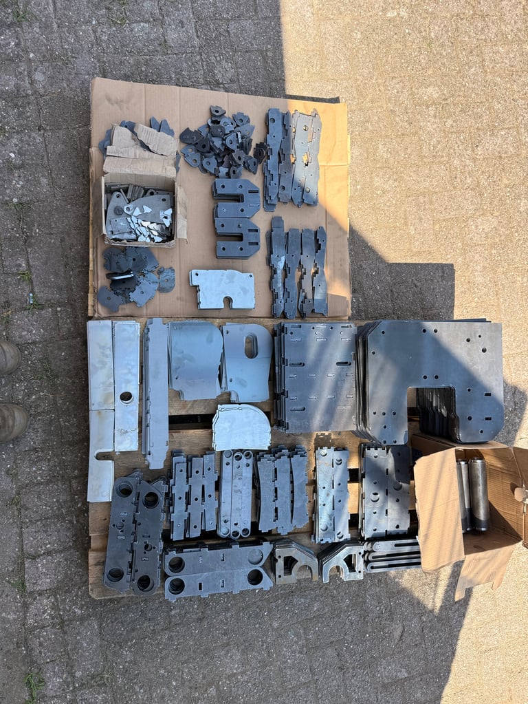 Overhead view of organized injection molded plastic parts and metal components laid out on cardboard pallets on pavement