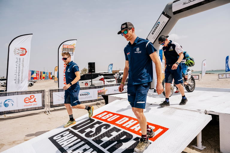 Runner crossing finish line at outdoor racing event with spectators and branded banners in background